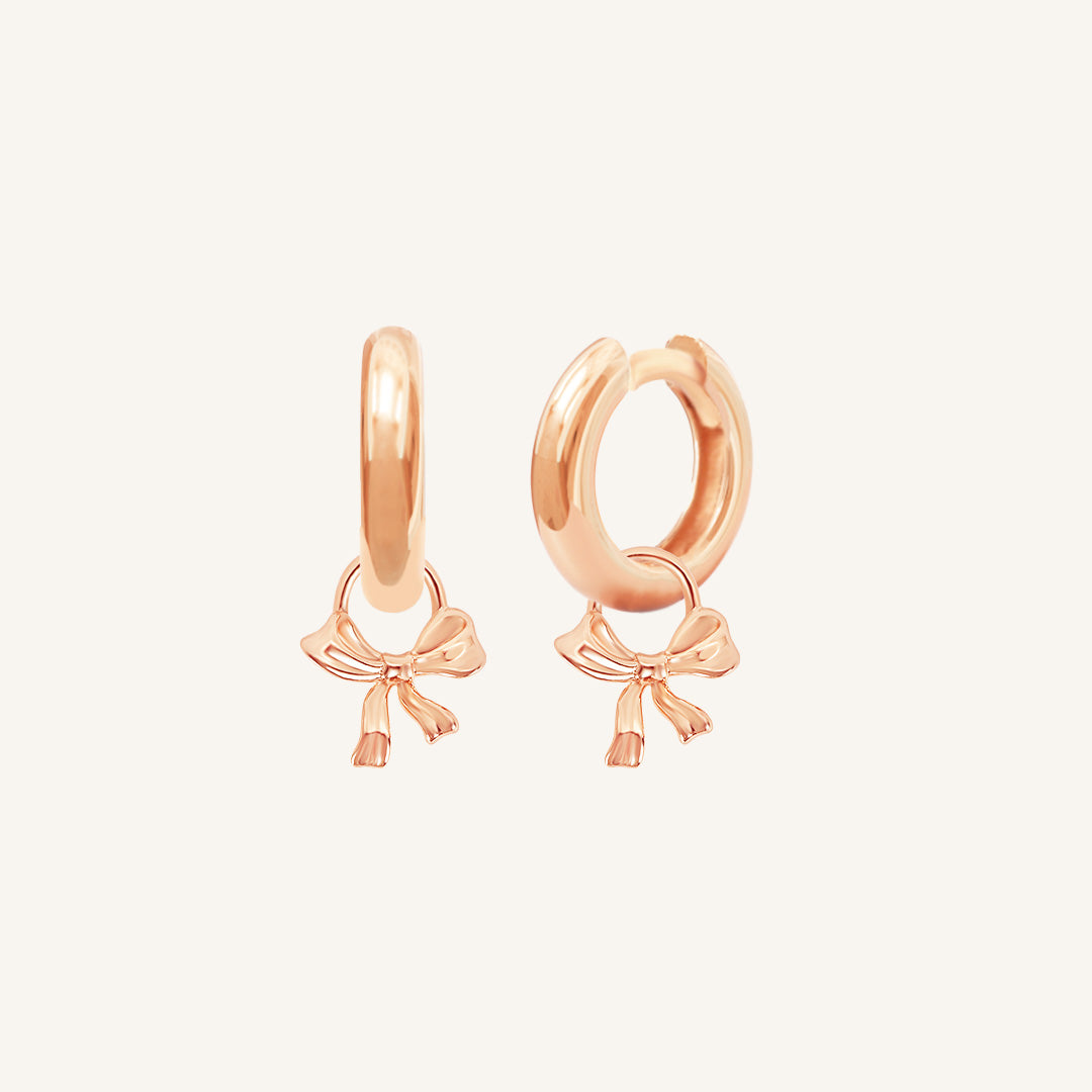A pair of rose-colored hoop earrings with charm pendants attached to them, displayed against a white background.