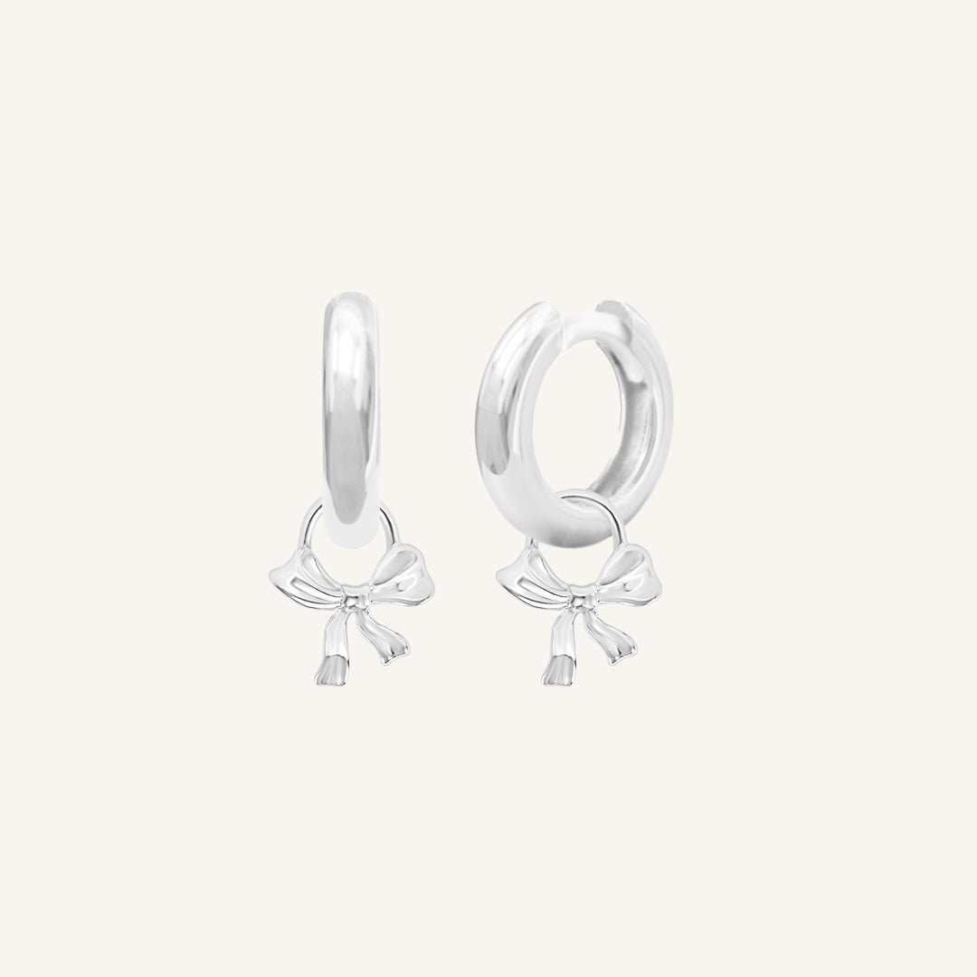 A pair of silver-coloured hoop earrings with charm pendants attached to them, displayed against a white background.