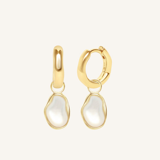 Gold hoop earrings with white teardrop-shaped charms on a light beige background