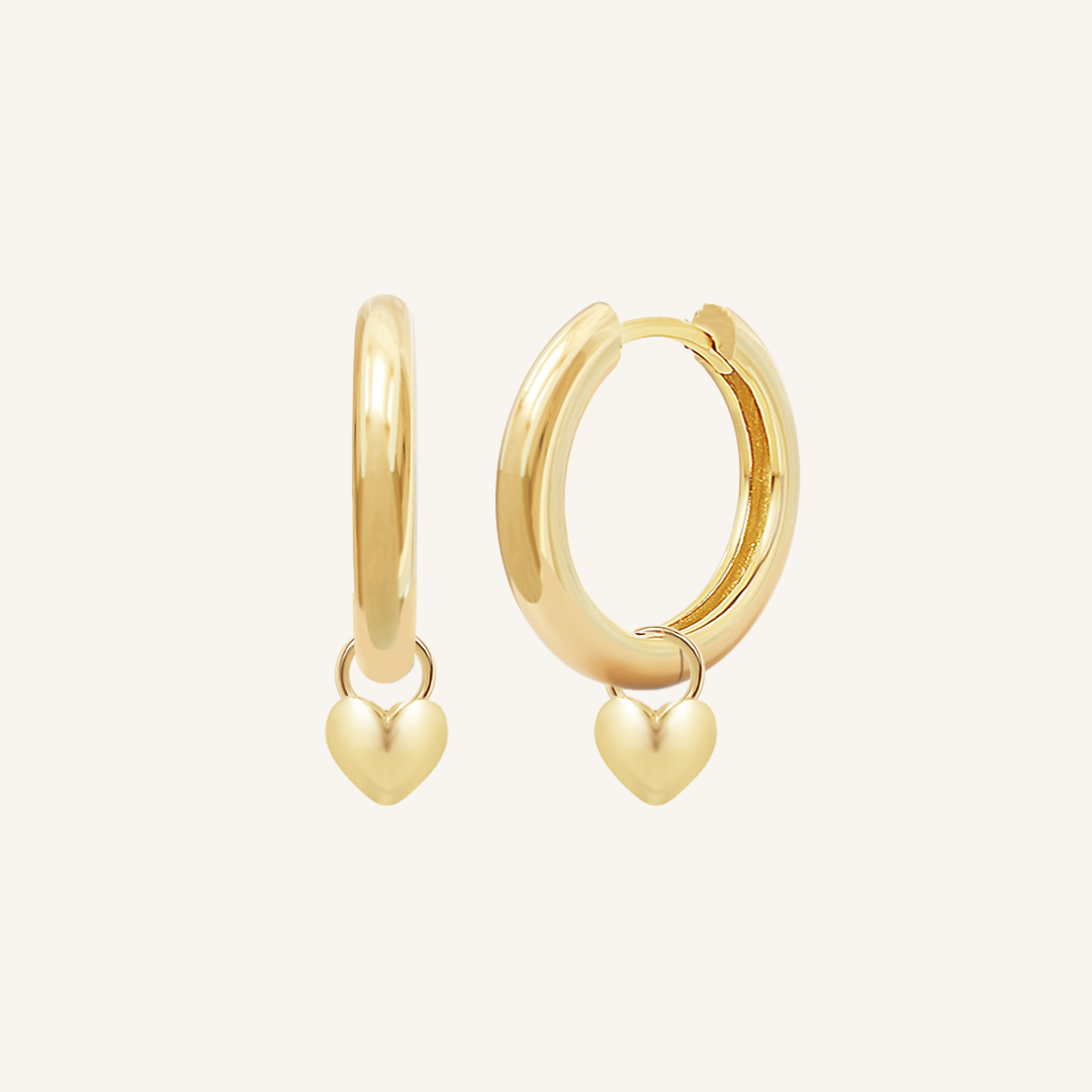 A pair of gold-colored hoop earrings with a dangling heart charm.