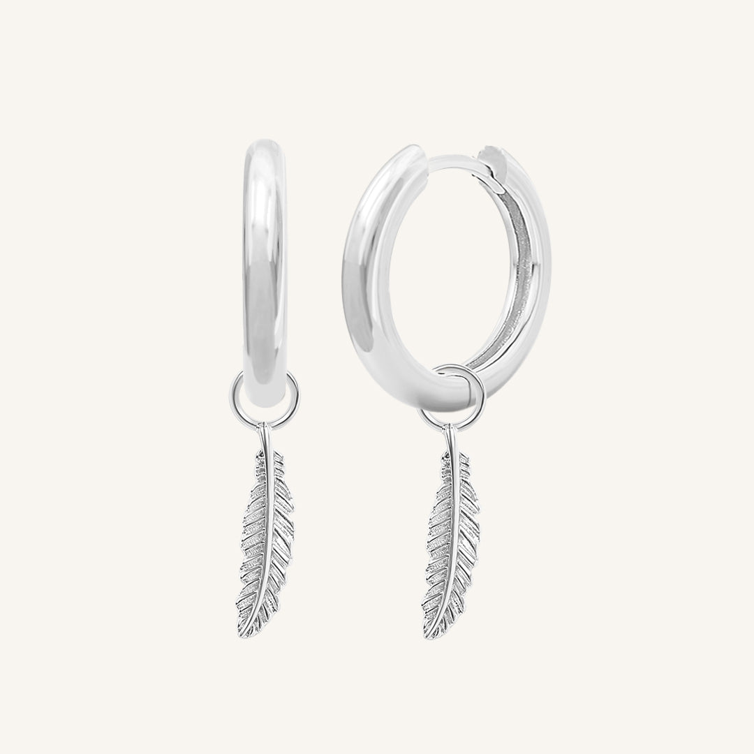 A pair of gold-colored hoop earrings with delicate feathers attached to the hoops.