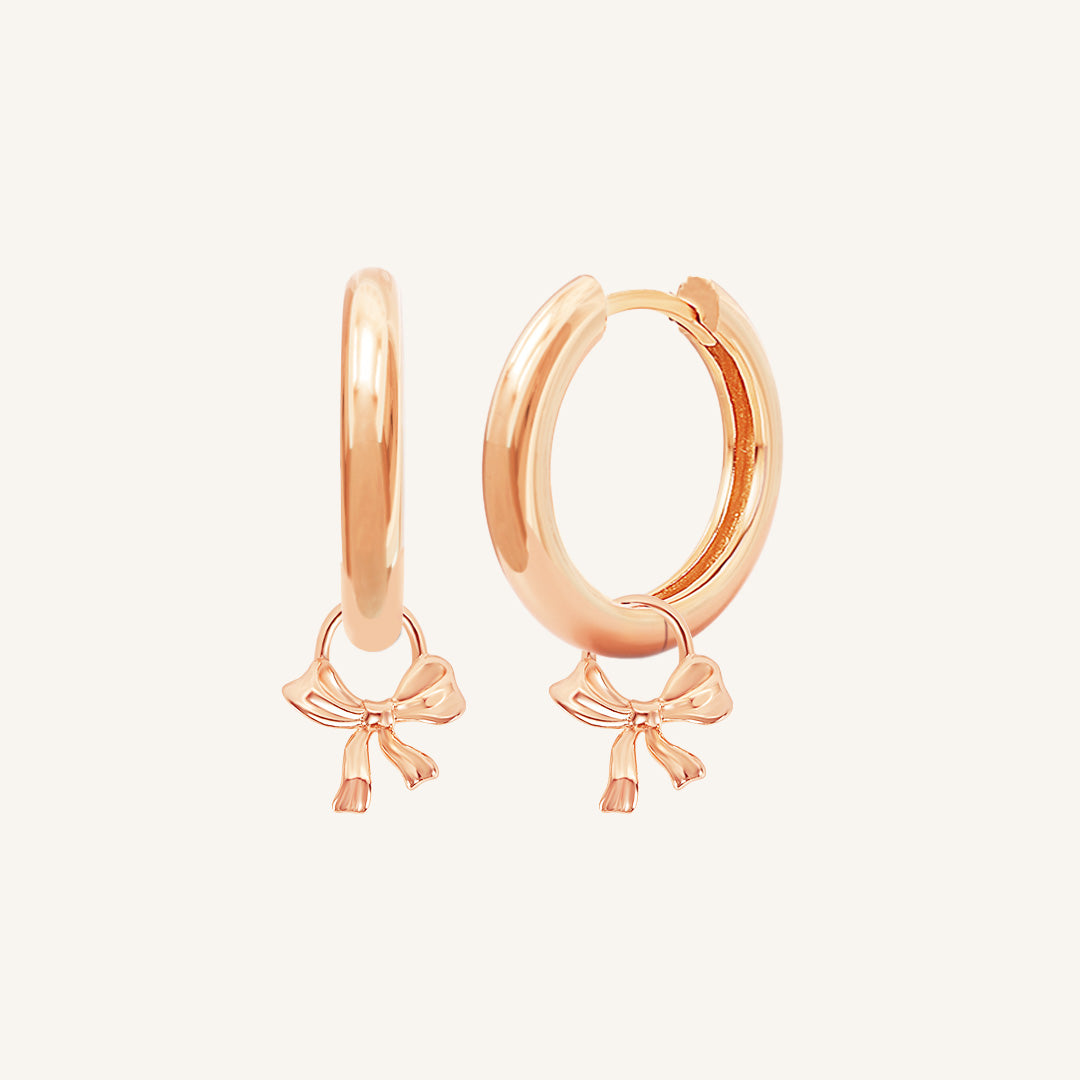 A pair of rose-colored hoop earrings with charm pendants attached to them, displayed against a white background.