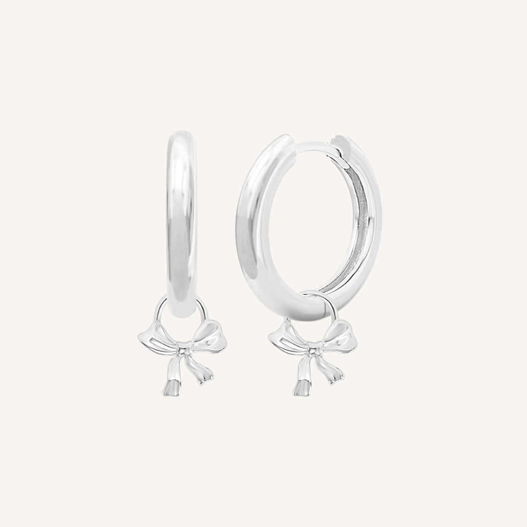 A pair of silver-colored hoop earrings with charm pendants attached to them, displayed against a white background.