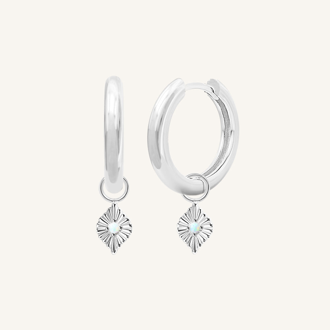 A pair of silver hoops with diamond shaped hoop charms featuring a faux opal