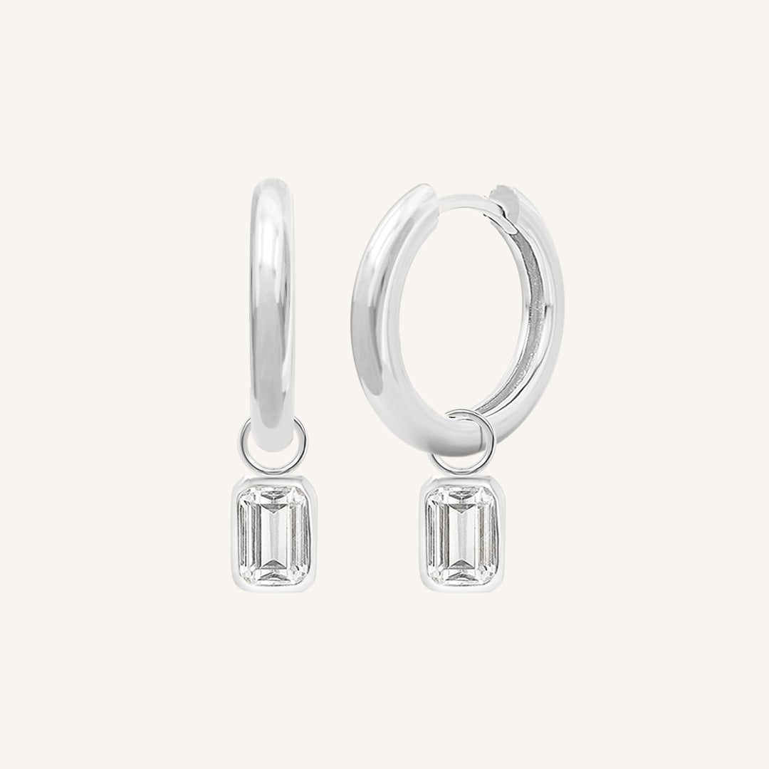 A pair of silver-colored hoop earrings with transparent crystal embellishments.