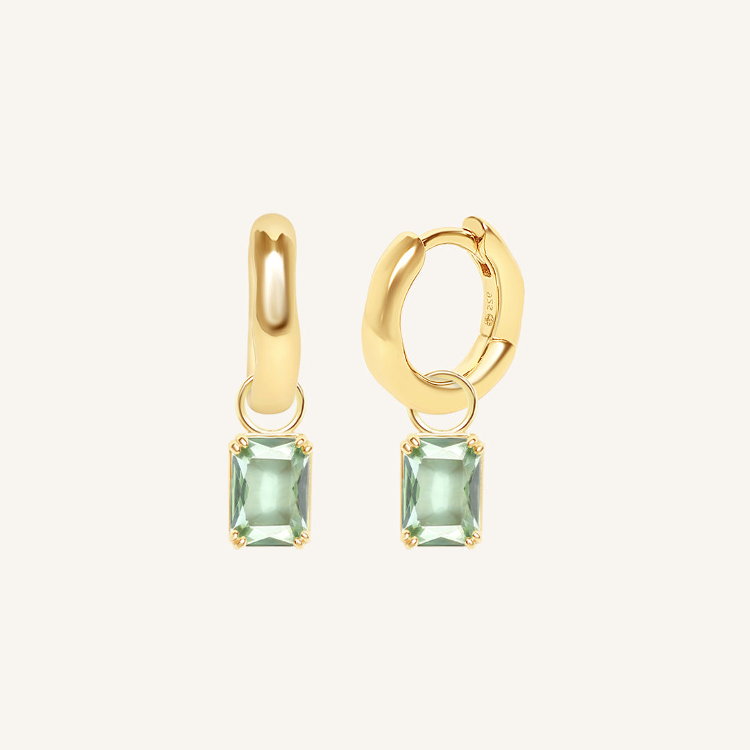 Gold hoop earrings with green gemstones on a white background