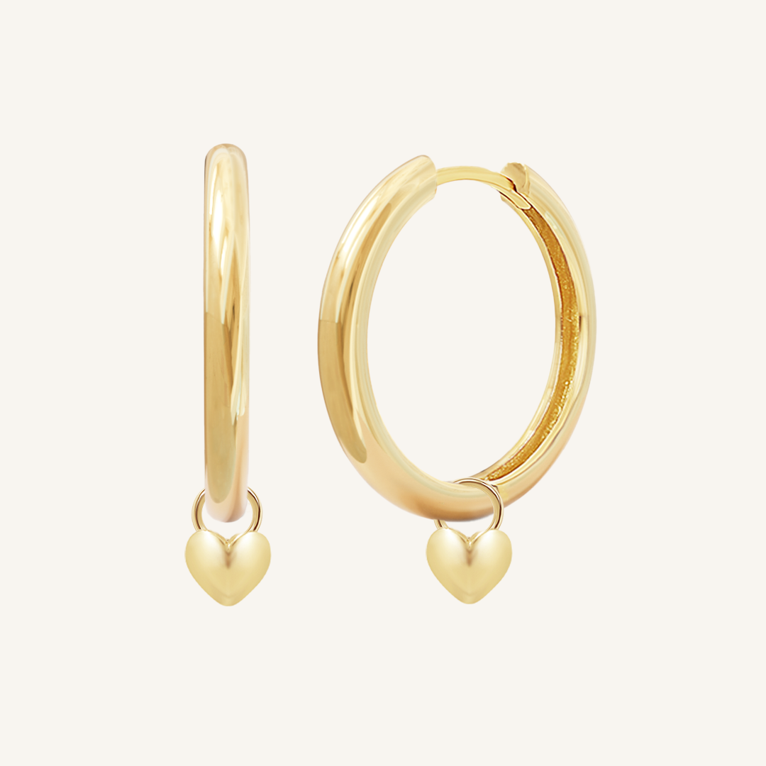 A pair of gold-colored hoop earrings with a dangling heart charm.