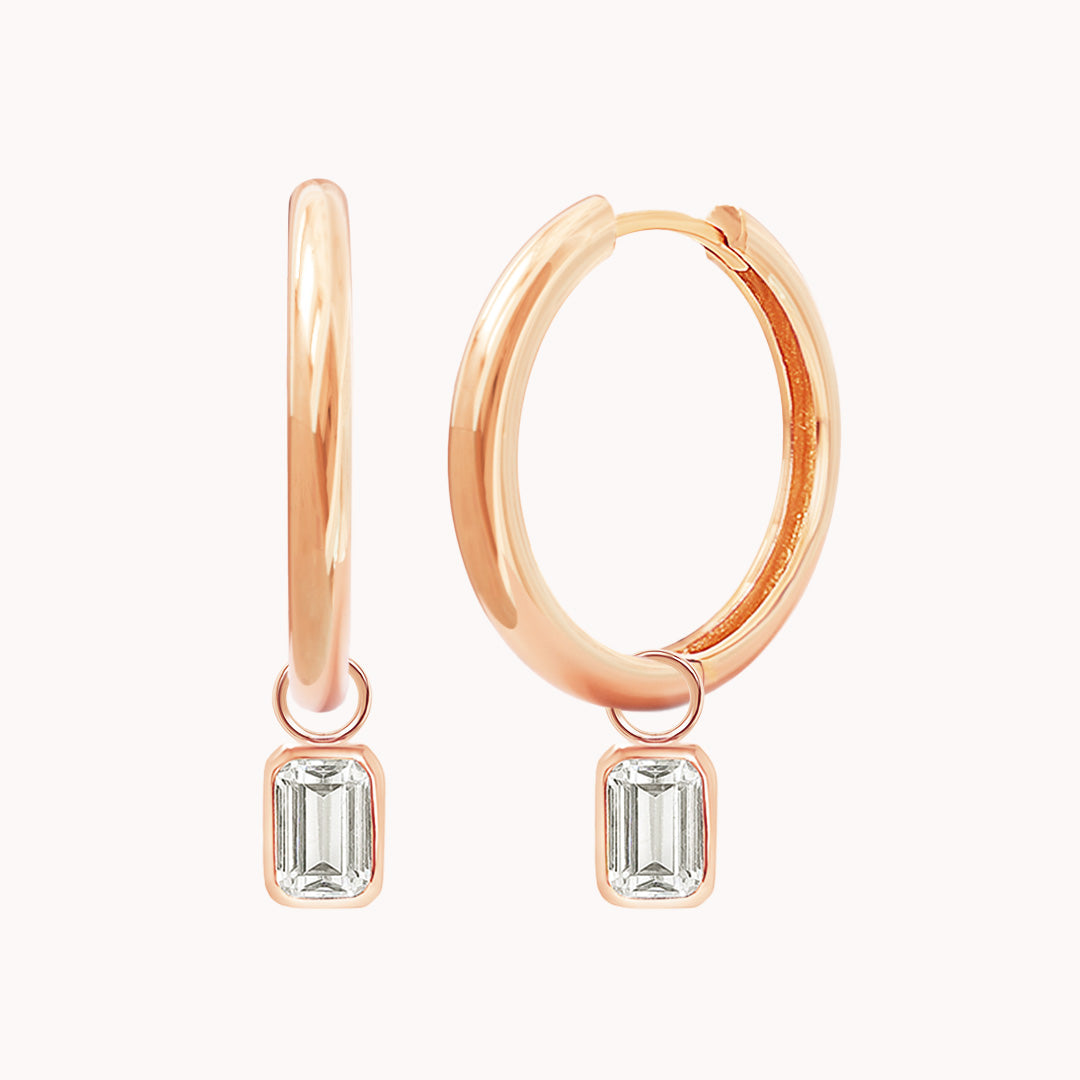 A pair of rose-colored hoop earrings with transparent crystal embellishments.