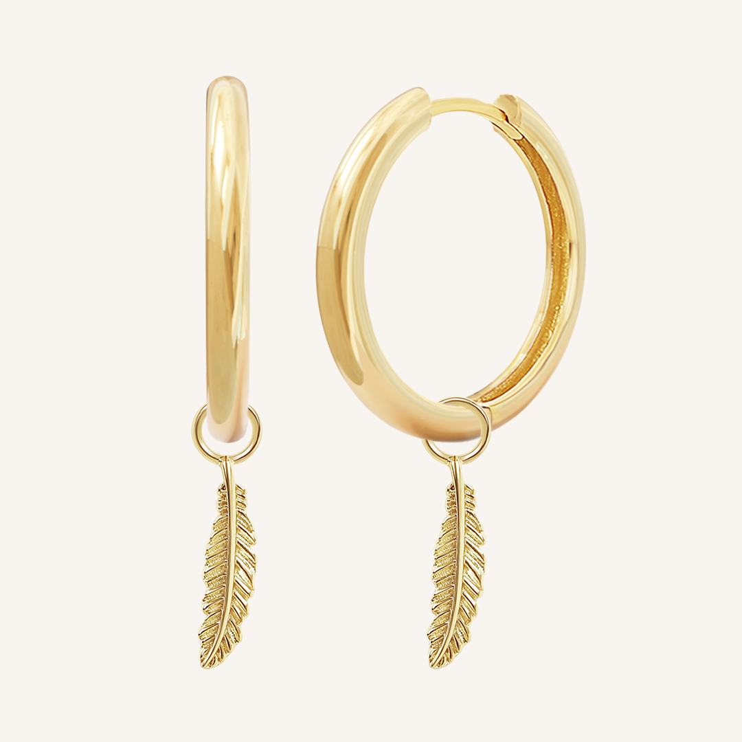A pair of gold hoop earrings with feather charms attached to them, displayed against a white background.
