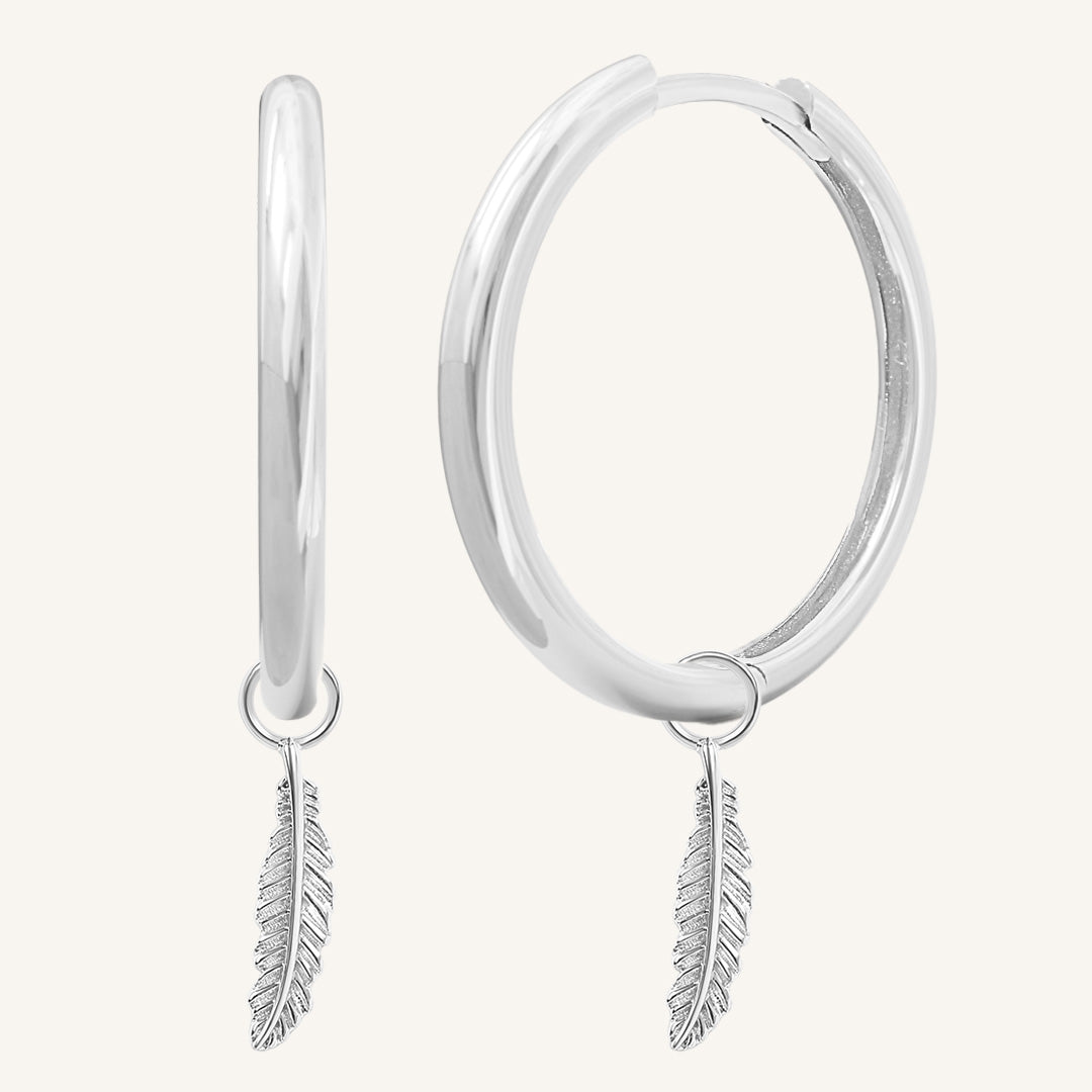 A pair of silver-coloured hoop earrings with delicate feathers attached to the hoops.