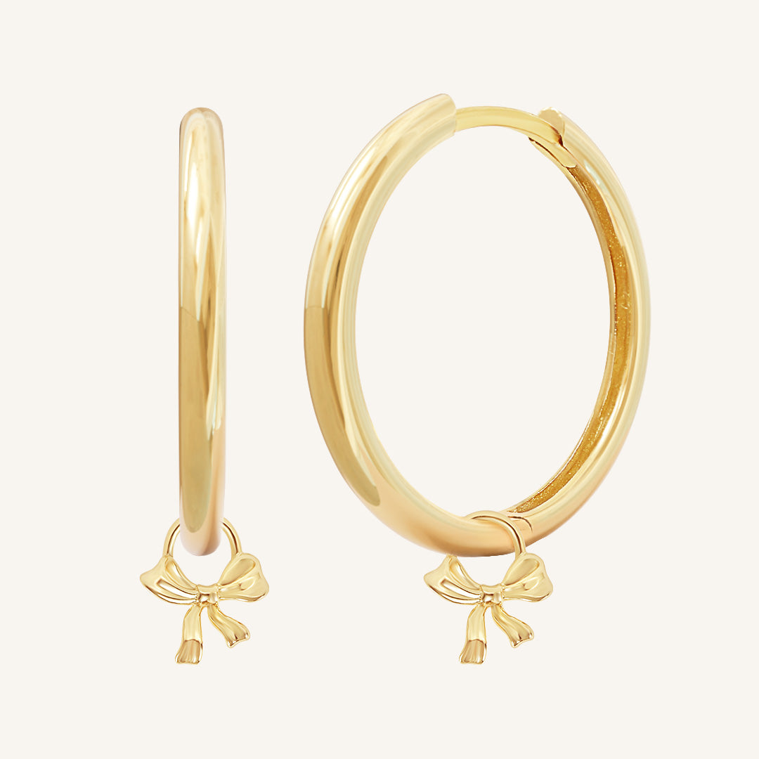 A pair of gold-colored hoop earrings with charm pendants attached to them, displayed against a white background.