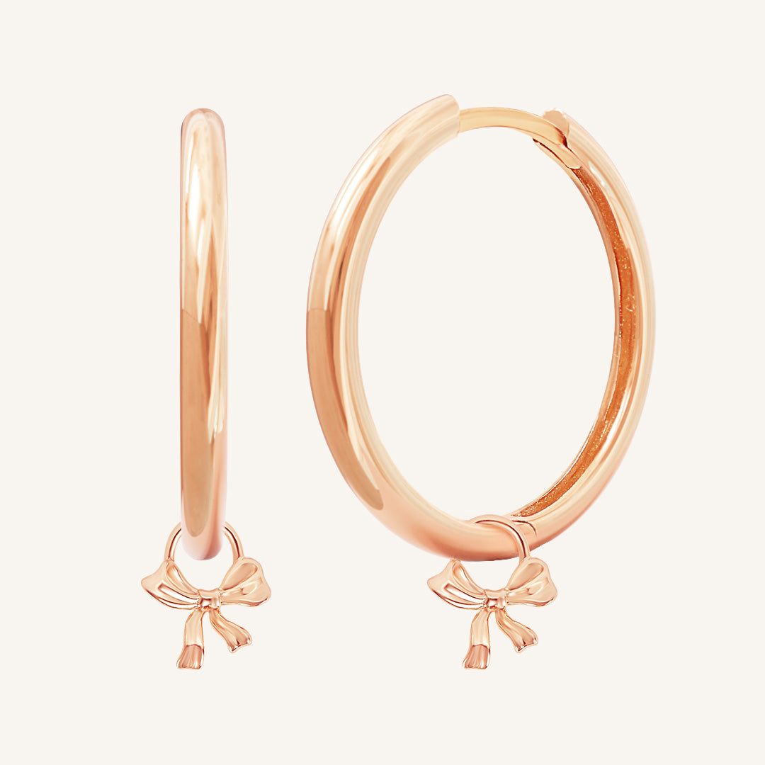 A pair of rose-colored hoop earrings with charm pendants attached to them, displayed against a white background.