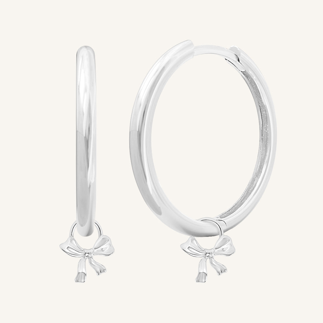 A pair of silver-colored hoop earrings with charm pendants attached to them, displayed against a white background.
