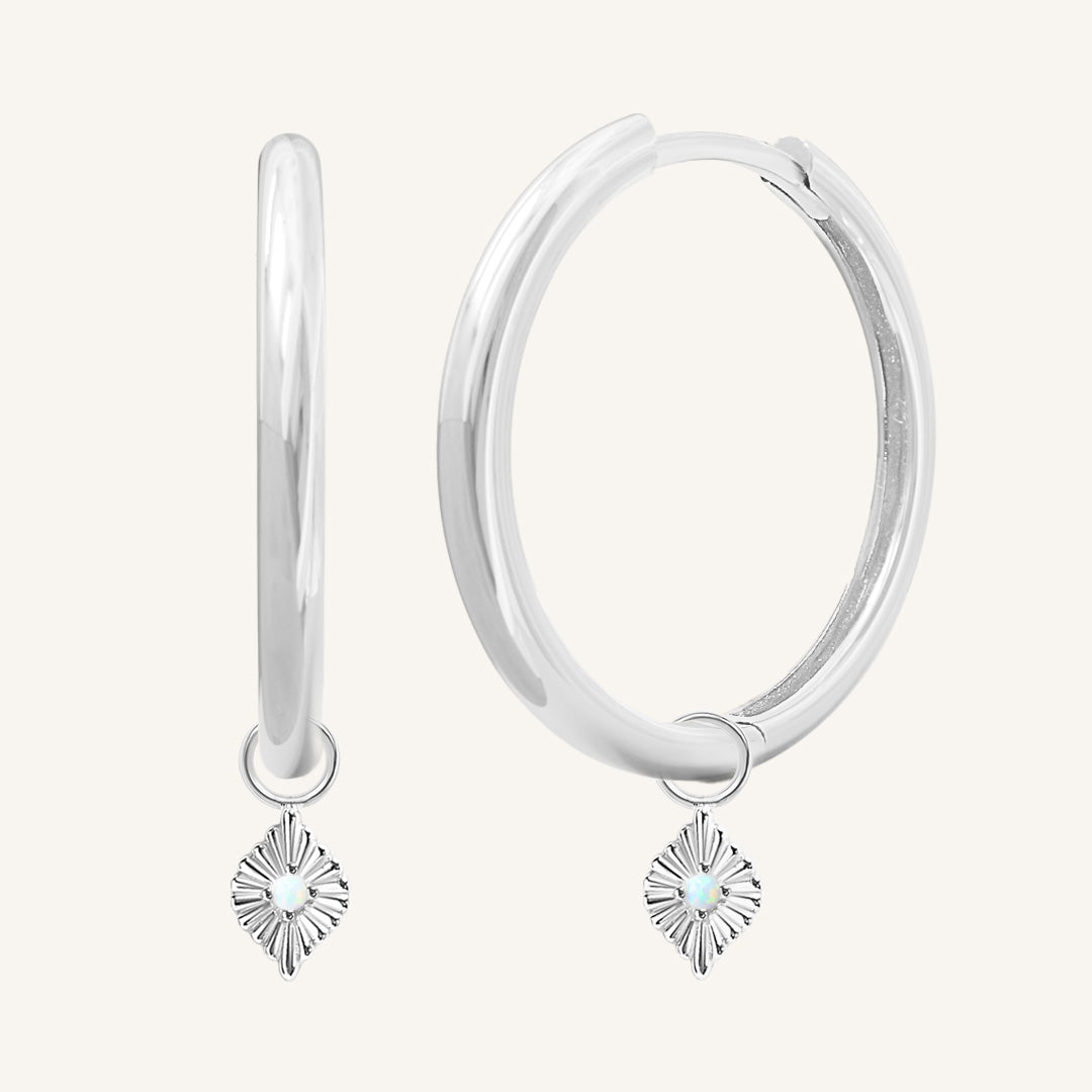 A pair of silver hoops with diamond shaped hoop charms featuring a faux opal