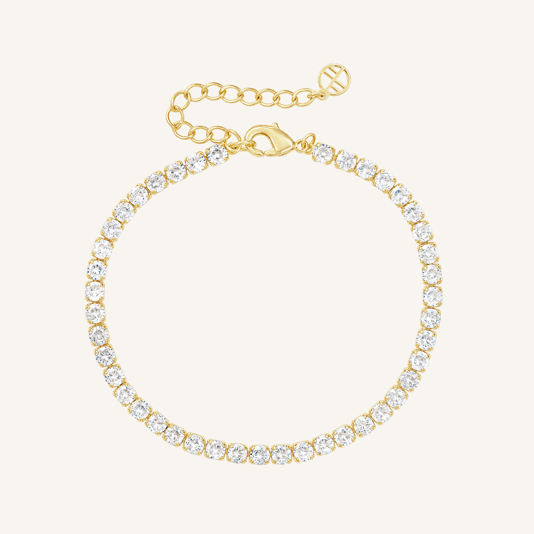 A gold-coloured tennis bracelet with clear cubic zirconias linked together, featuring a extender chain for adjustable length.