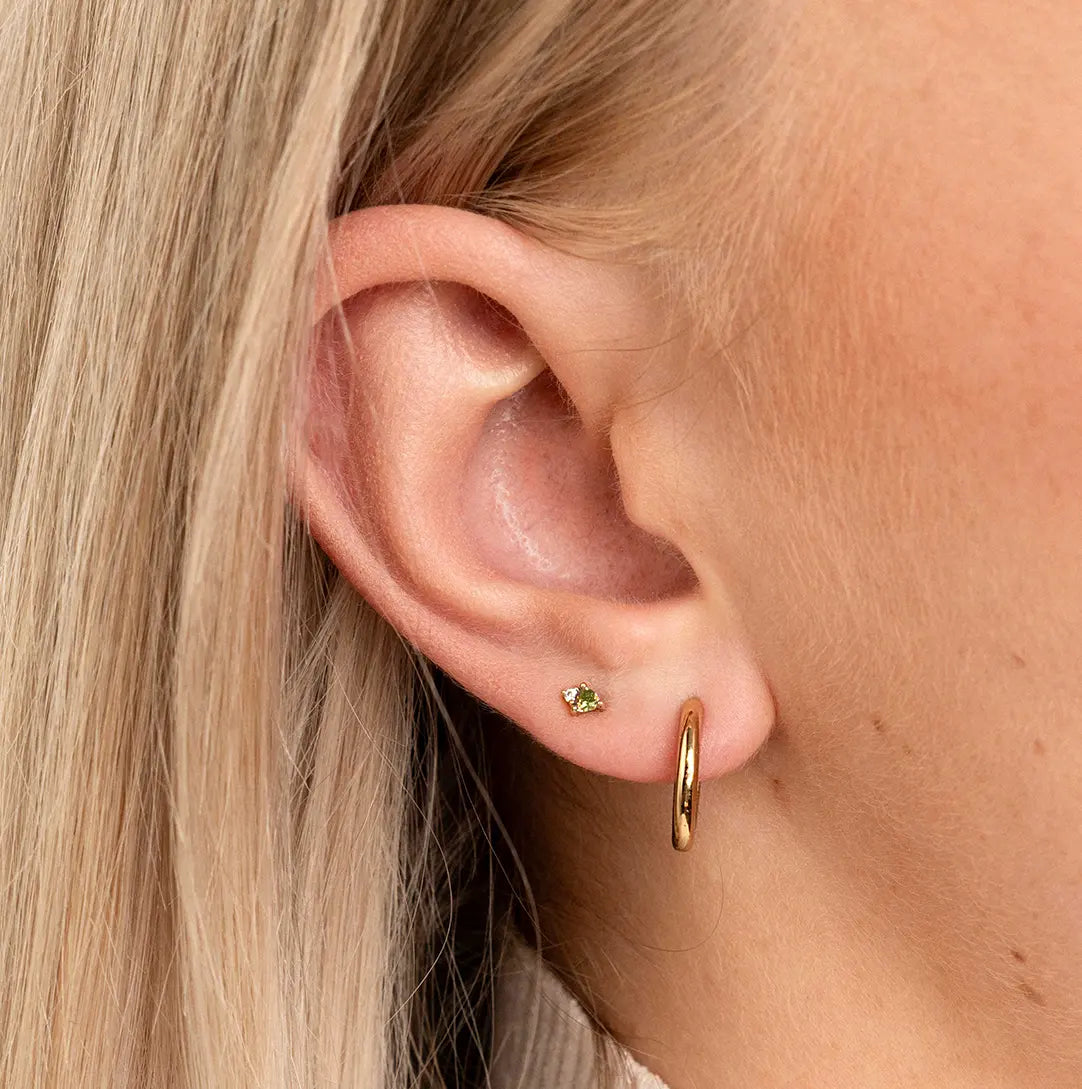 A silver stud earring featuring a green cubic zirconia, representing August, close up in ear.