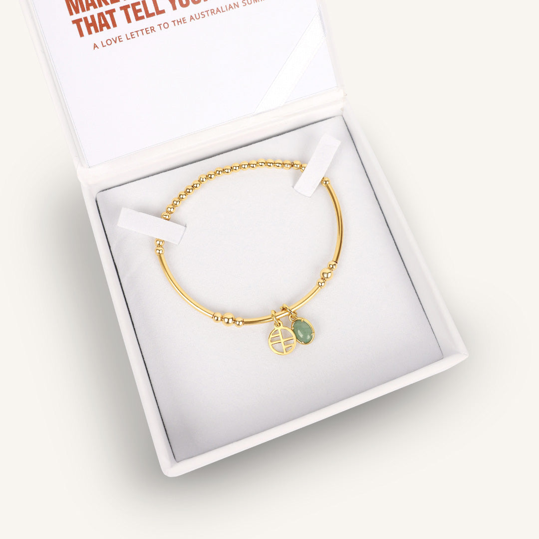 Gold bracelet with a green gemstone charm in a white box