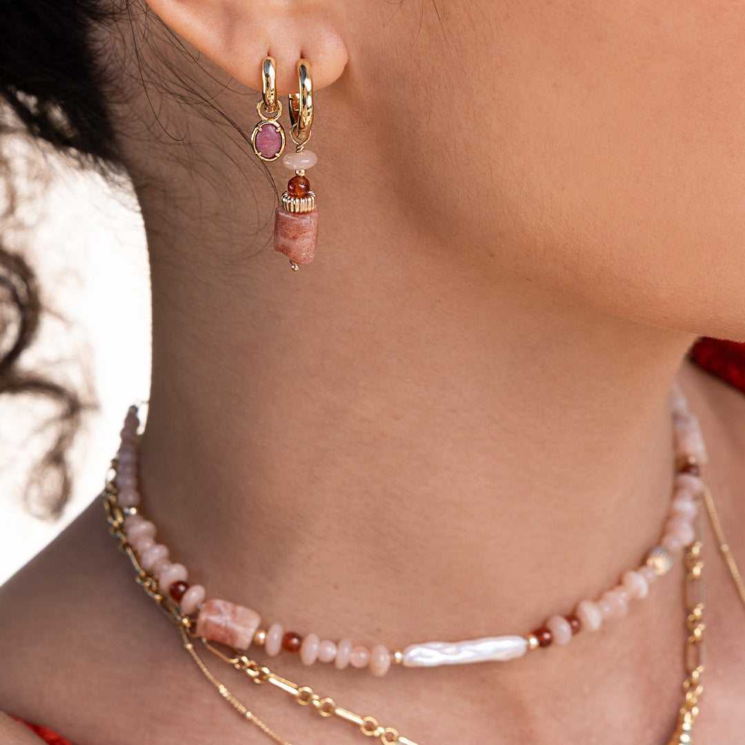 Close-up of a person wearing gold hoop earrings with pink and red beads and a matching necklace.