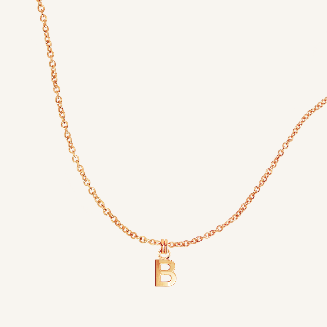 Gold necklace with a 'B' pendant on a light beige background