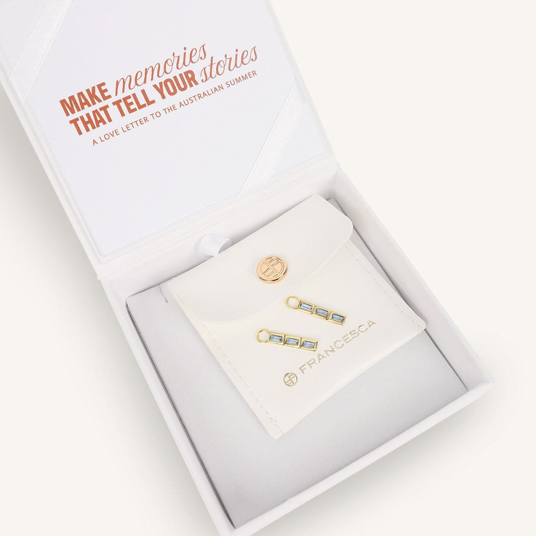 Gold hoop charms with blue gemstones, displayed in white box