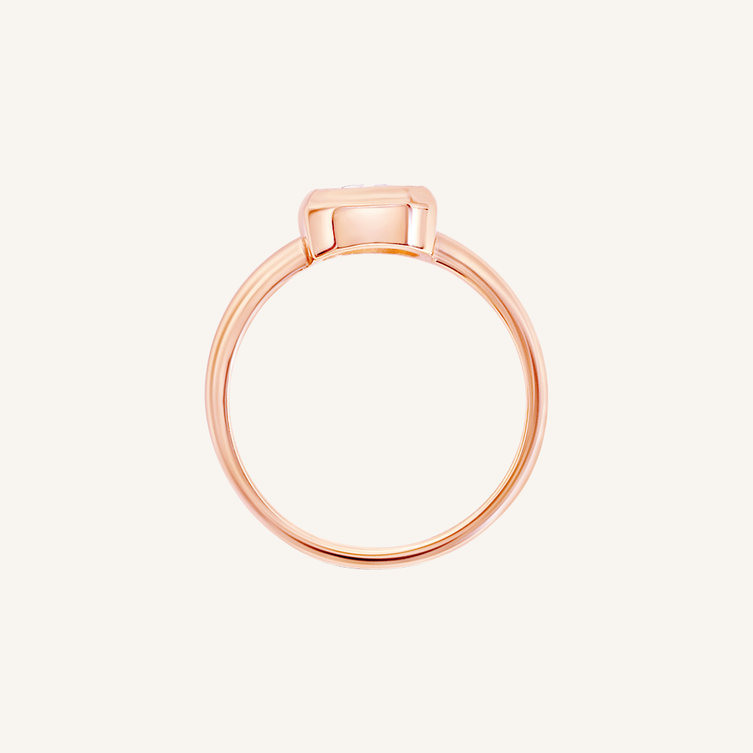 A rose gold-coloured ring with a white cubic zirconia, bezel set in a rectangular frame with a smooth, polished band, side profile