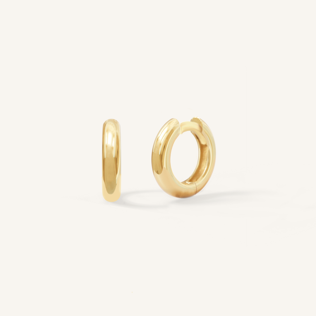A pair of gold-colored huggie hoop earrings on a white background.