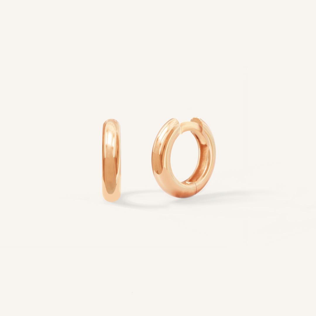 A pair of rose-colored huggie hoop earrings on a white background.