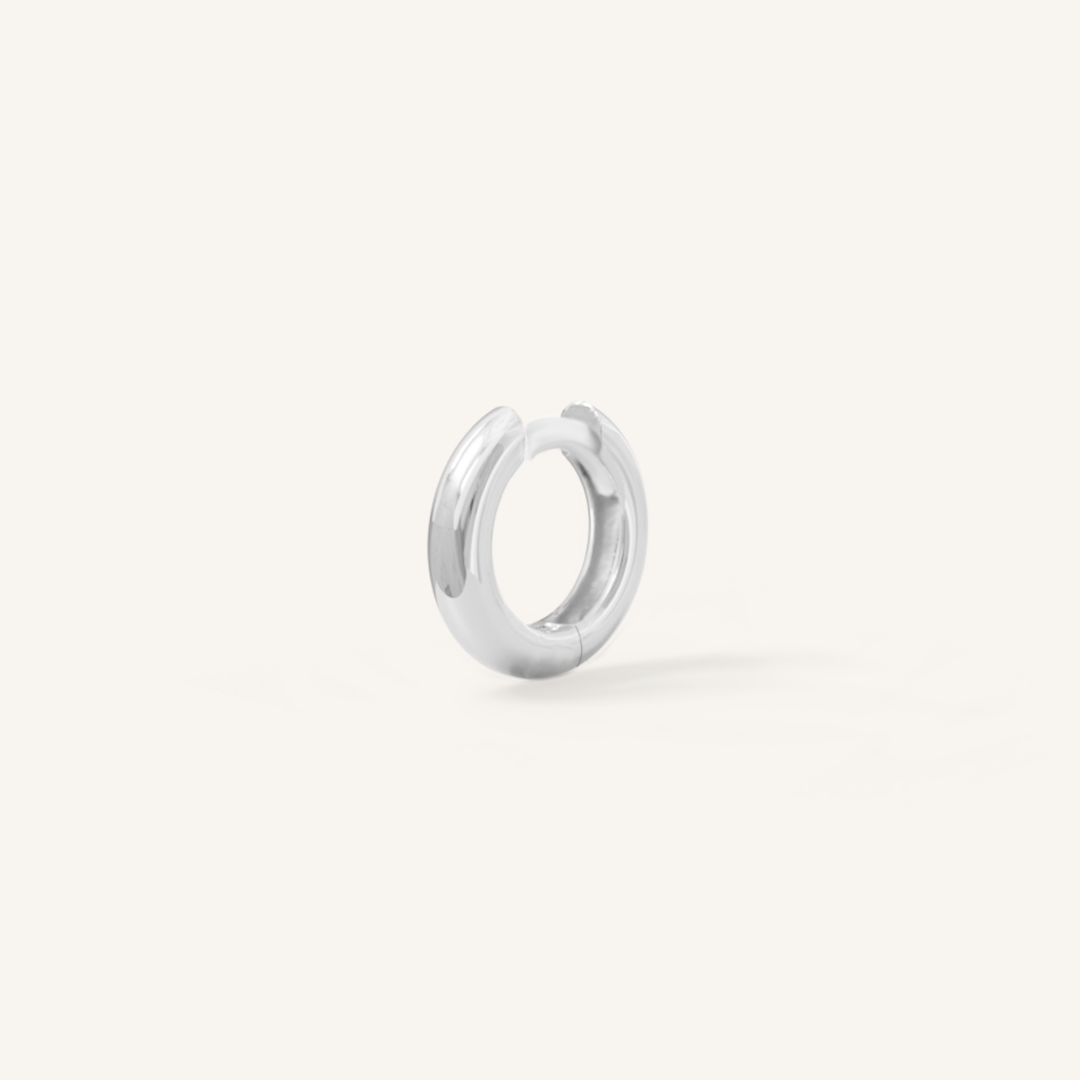 A silver huggie hoop earring on a white background.