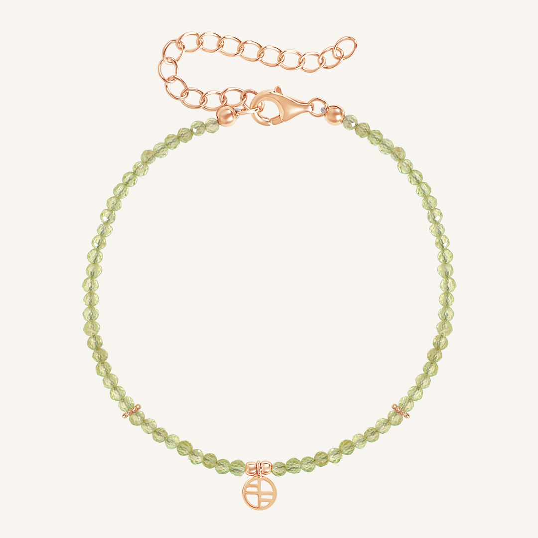 A beaded bracelet with green stones and a rose metal clasp, representing the August birthstone.