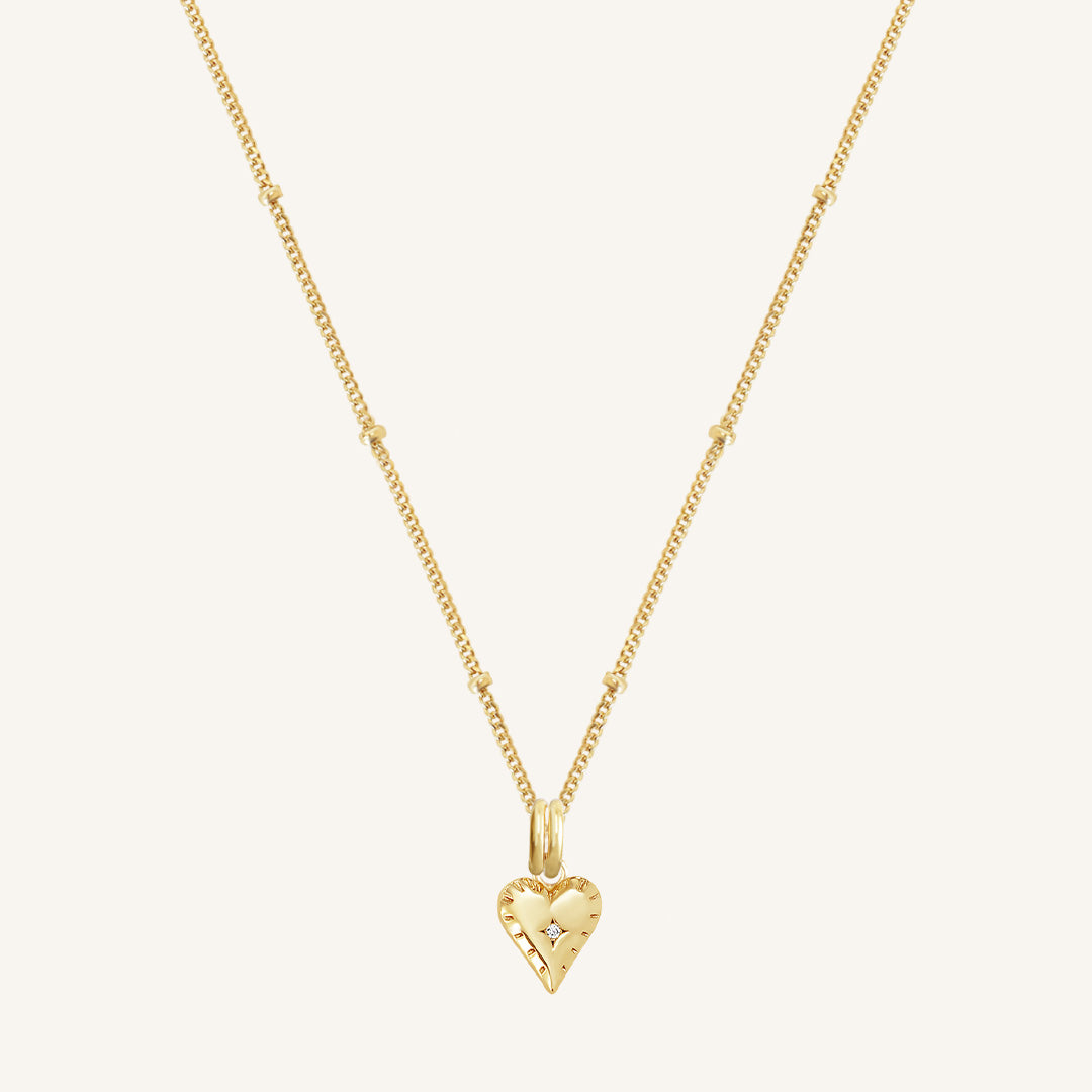 A gold-tone heart charm necklace with a fine chain, displayed against a white background.