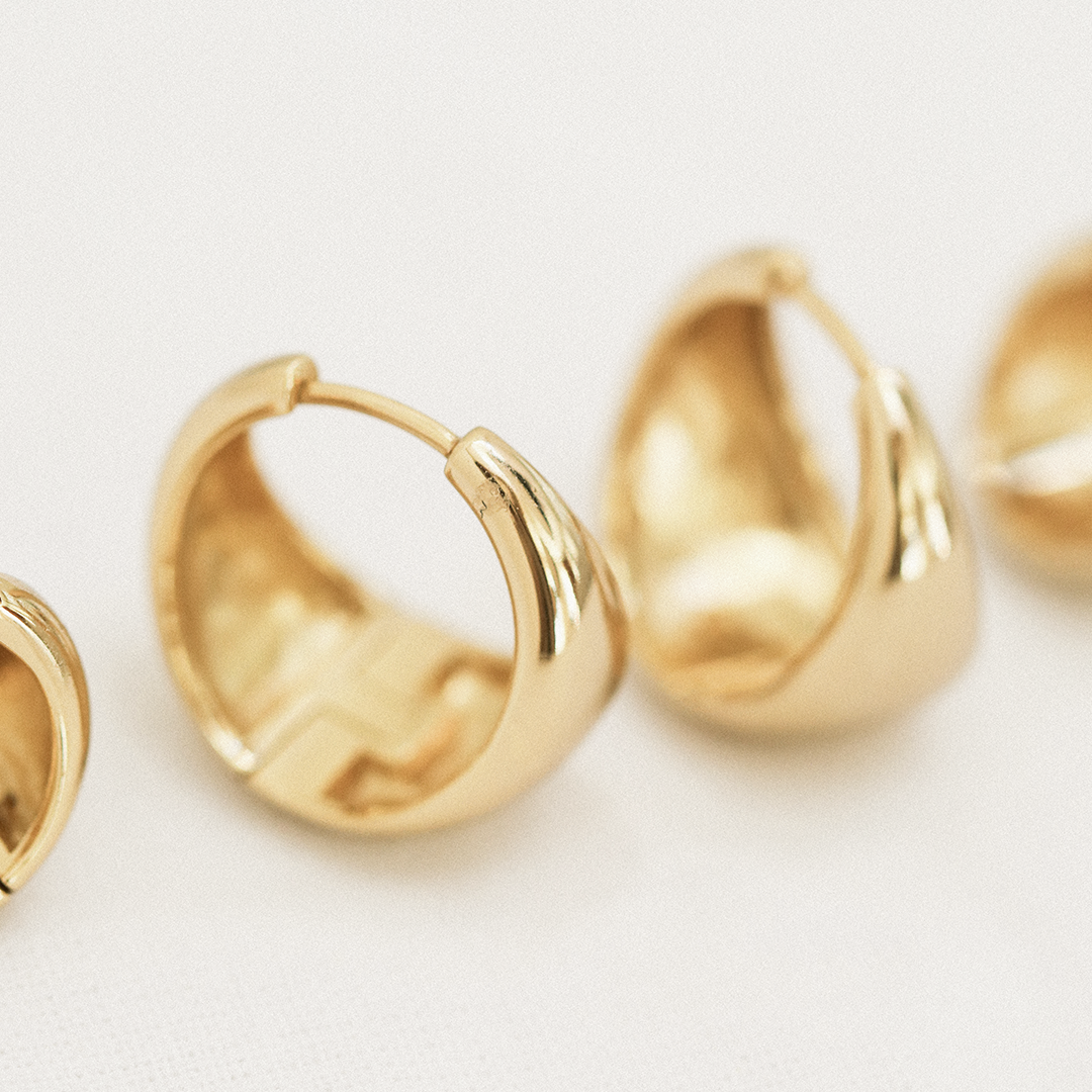 Close up of A pair of gold-colored chunky hoop earrings on a white background.