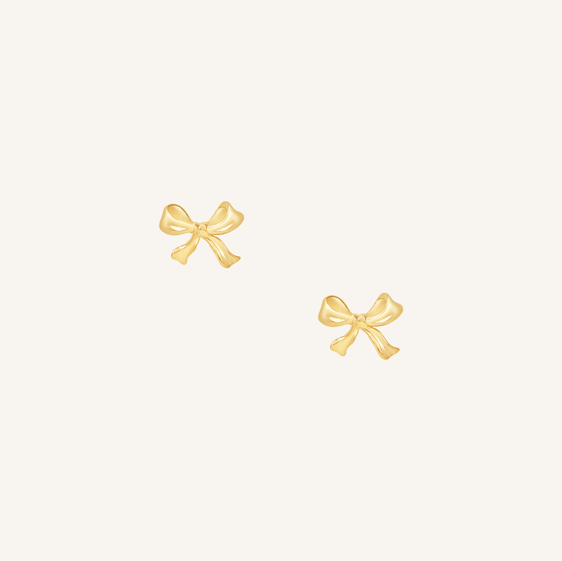 A pair of gold bow stud earrings on a white background