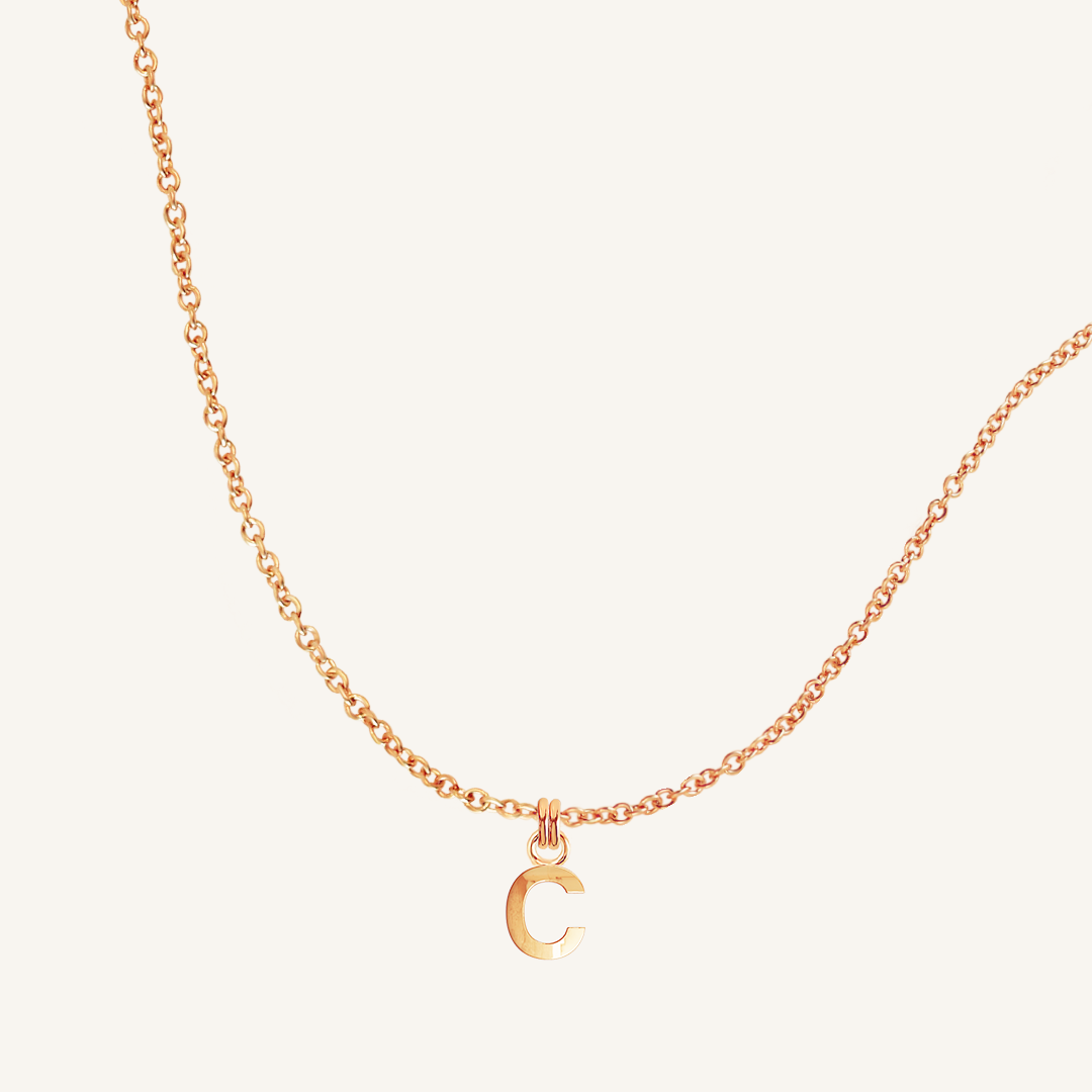 Rose gold necklace with a C pendant on a light beige background