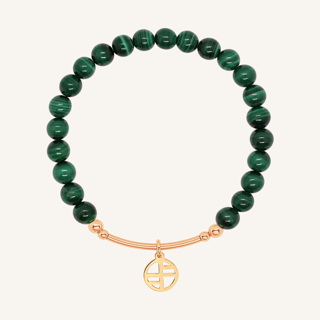 A beaded malachite charm bracelet with green stones and a rose-tone charm, displayed against a white background.