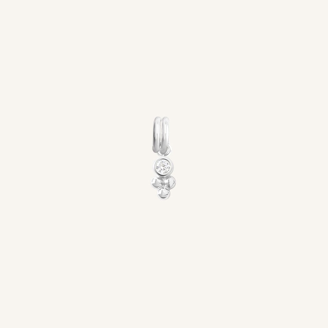 A small silver charm featuring a cubic zirconia and a floral design.