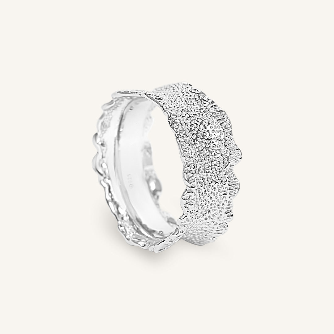 Silver ring with textured design on a white background