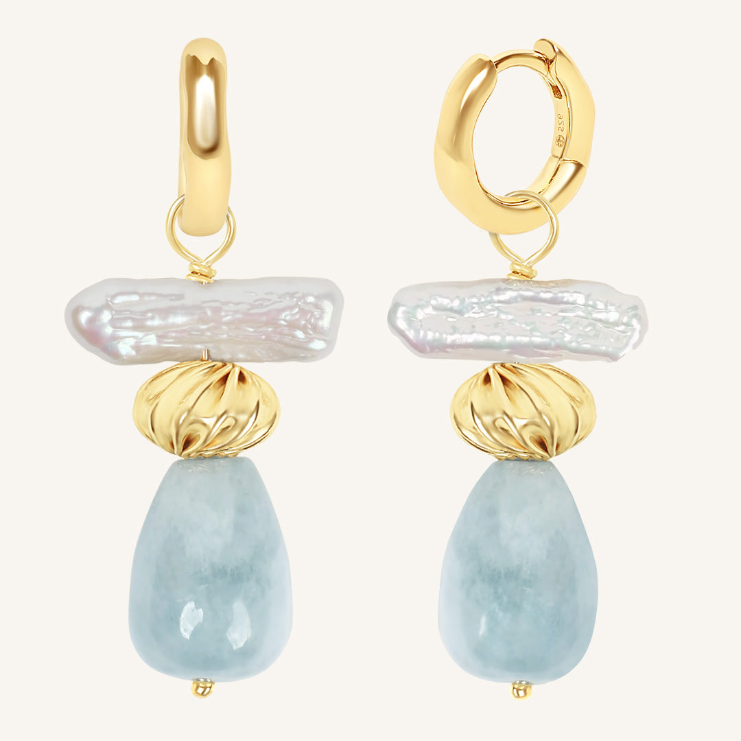 Gold hoop earrings with pearl and blue stone drops on a white background
