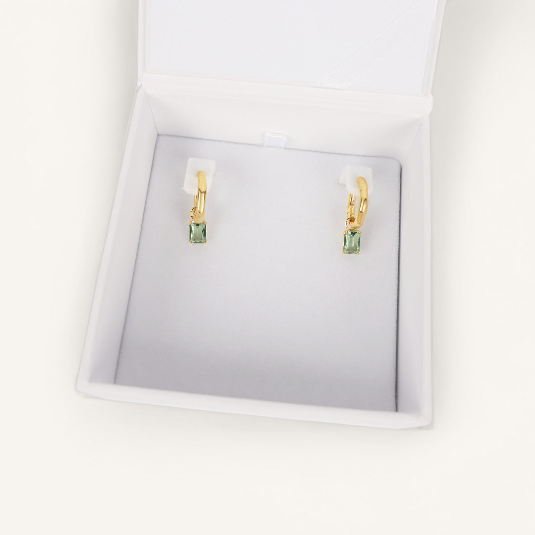 Gold earrings with green gemstones in a white box