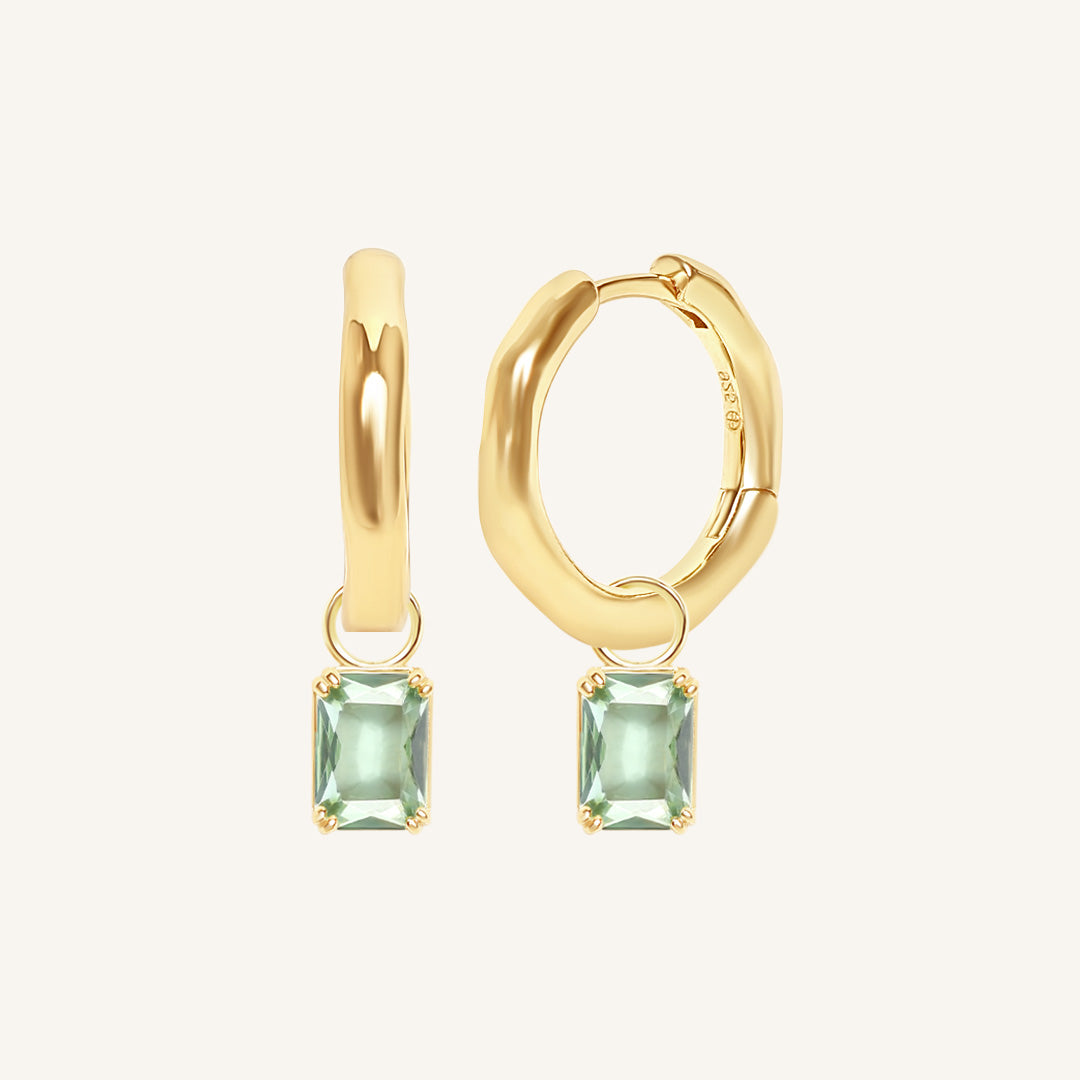Gold hoop earrings with green gemstones on a white background