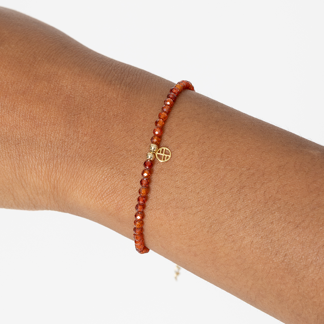 Beaded bracelet with a gold charm on a wrist against a white background