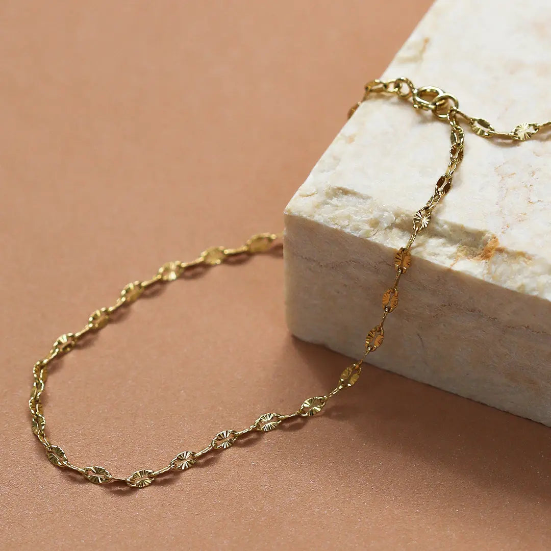 A gold-coloured metal chain anklet close up