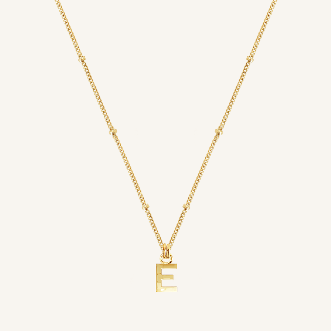 Gold necklace with a letter 'E' pendant on a light beige background