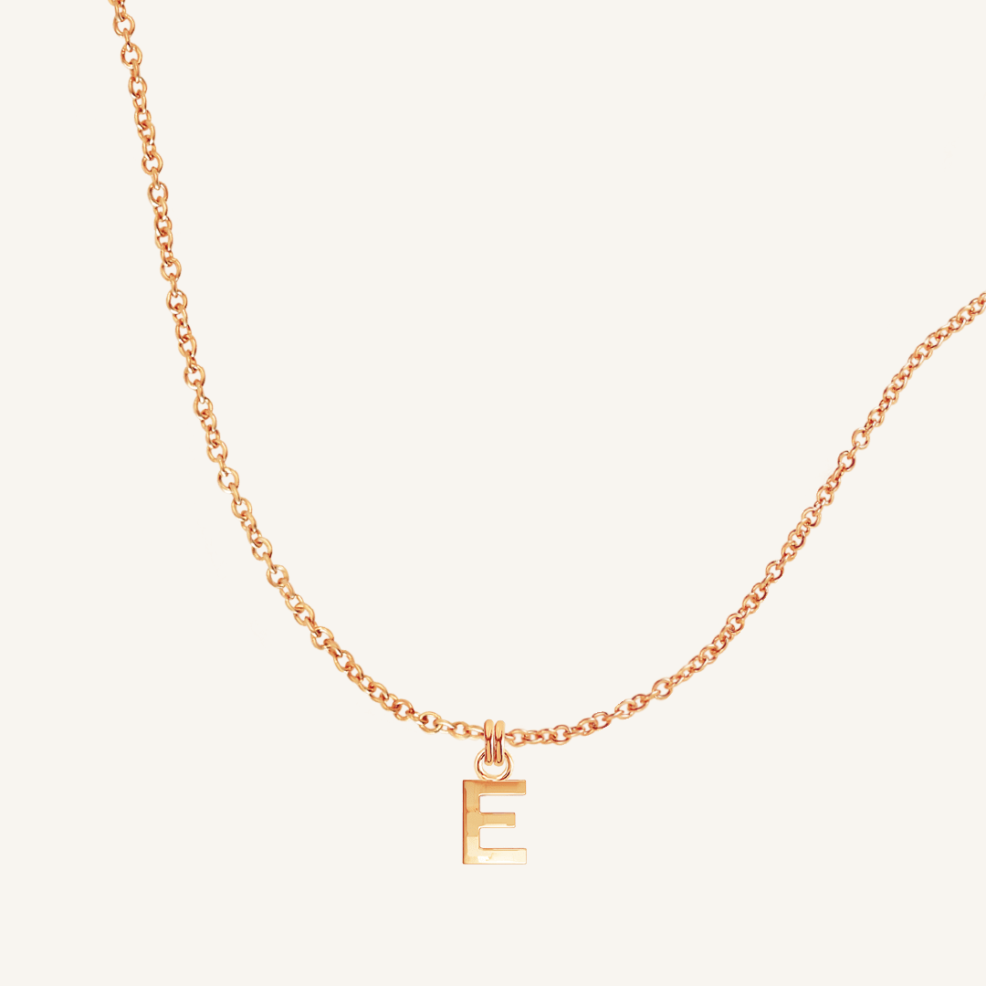 Rose gold necklace with a 'E' pendant on a light beige background