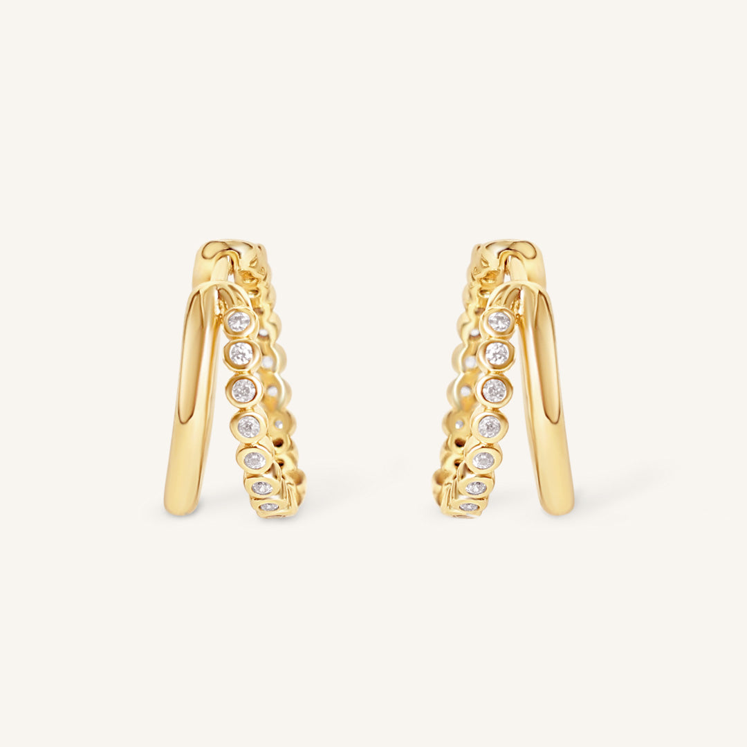 Gold hoop earrings with embedded diamonds on a light beige background