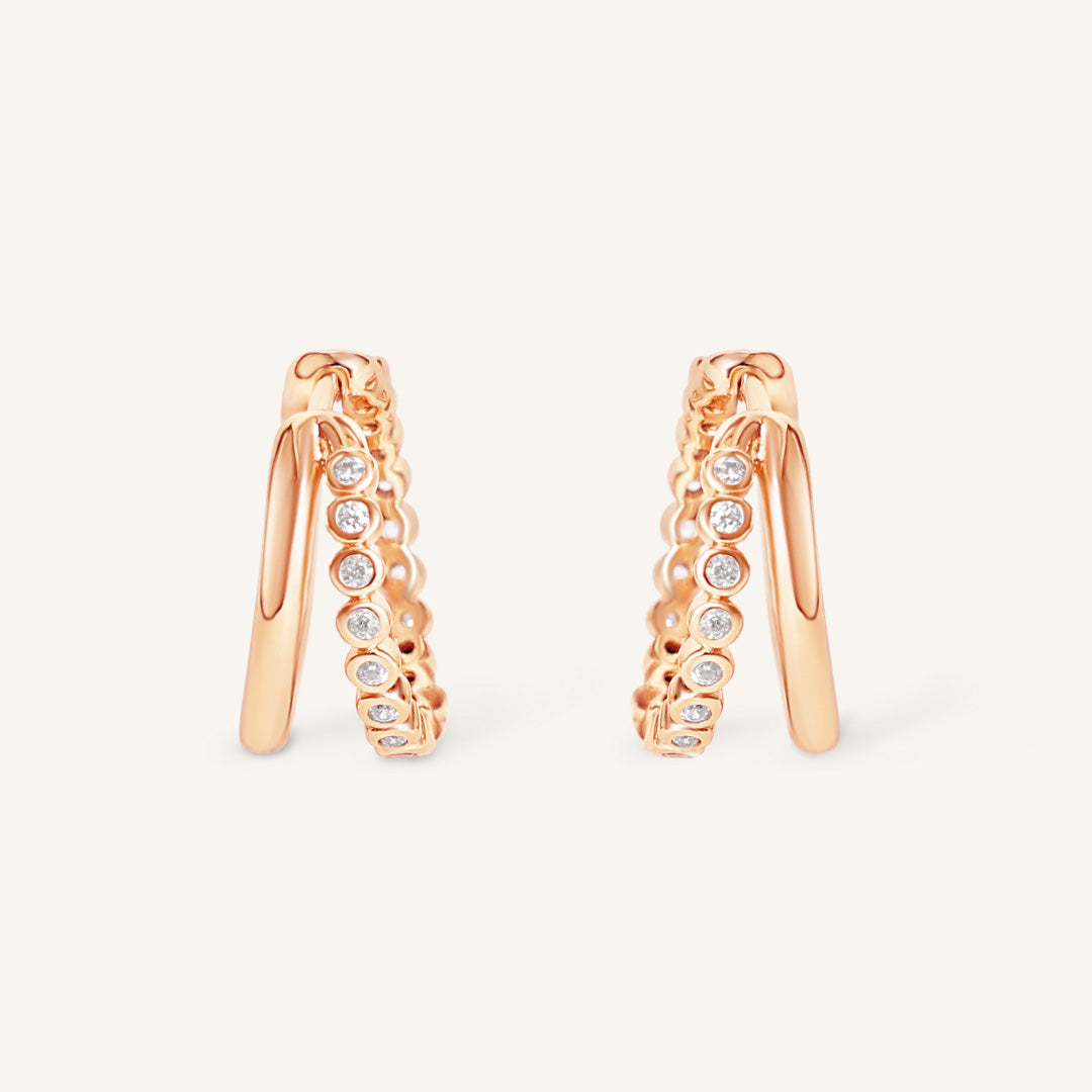 Rose gold hoop earrings with embedded diamonds on a light beige background