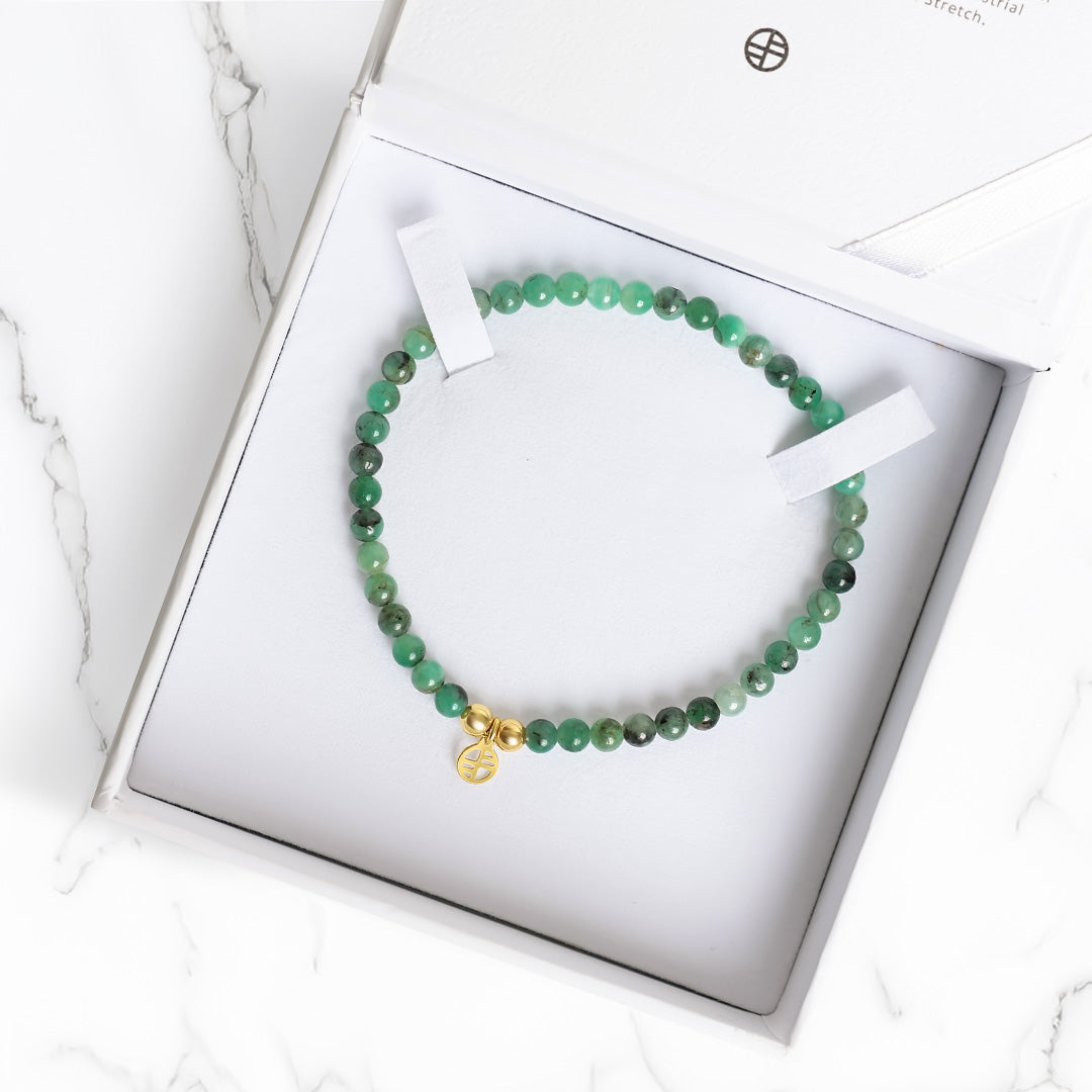 Green beaded bracelet with a gold charm in a white box on a marble surface