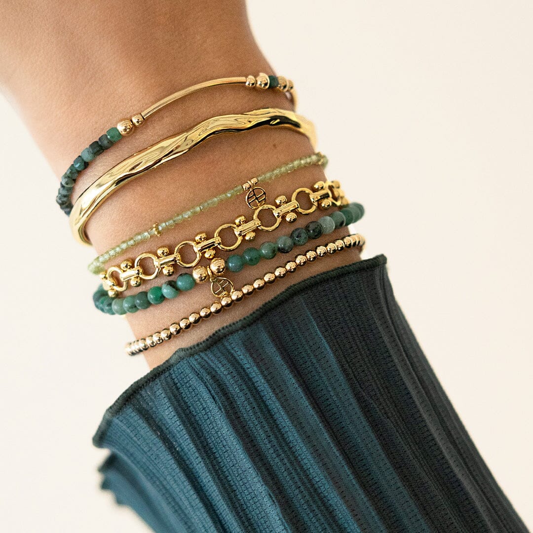 Stack of gold and green bracelets on a wrist with a blurred background