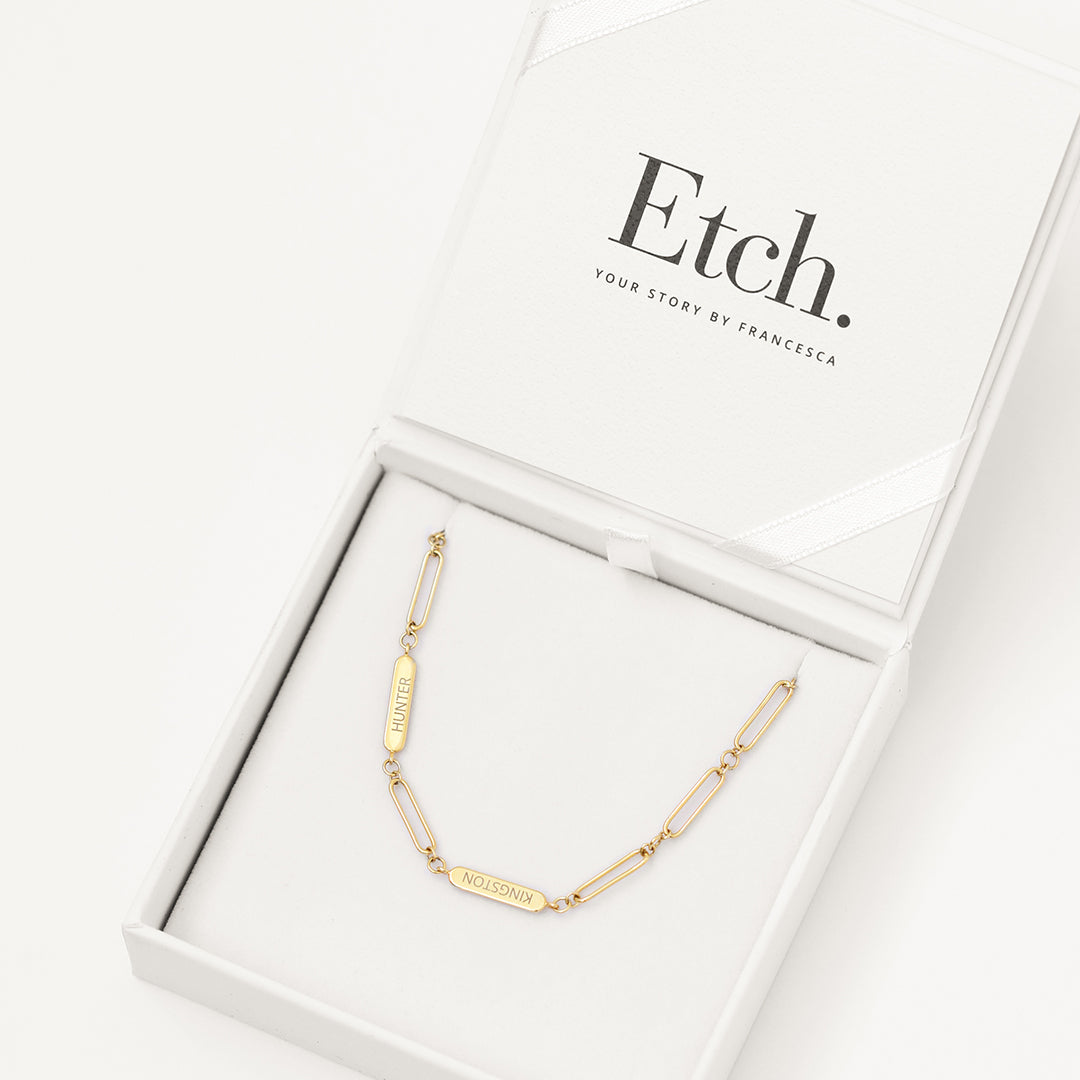 A gold chain necklace with two engraveable panels in white box
