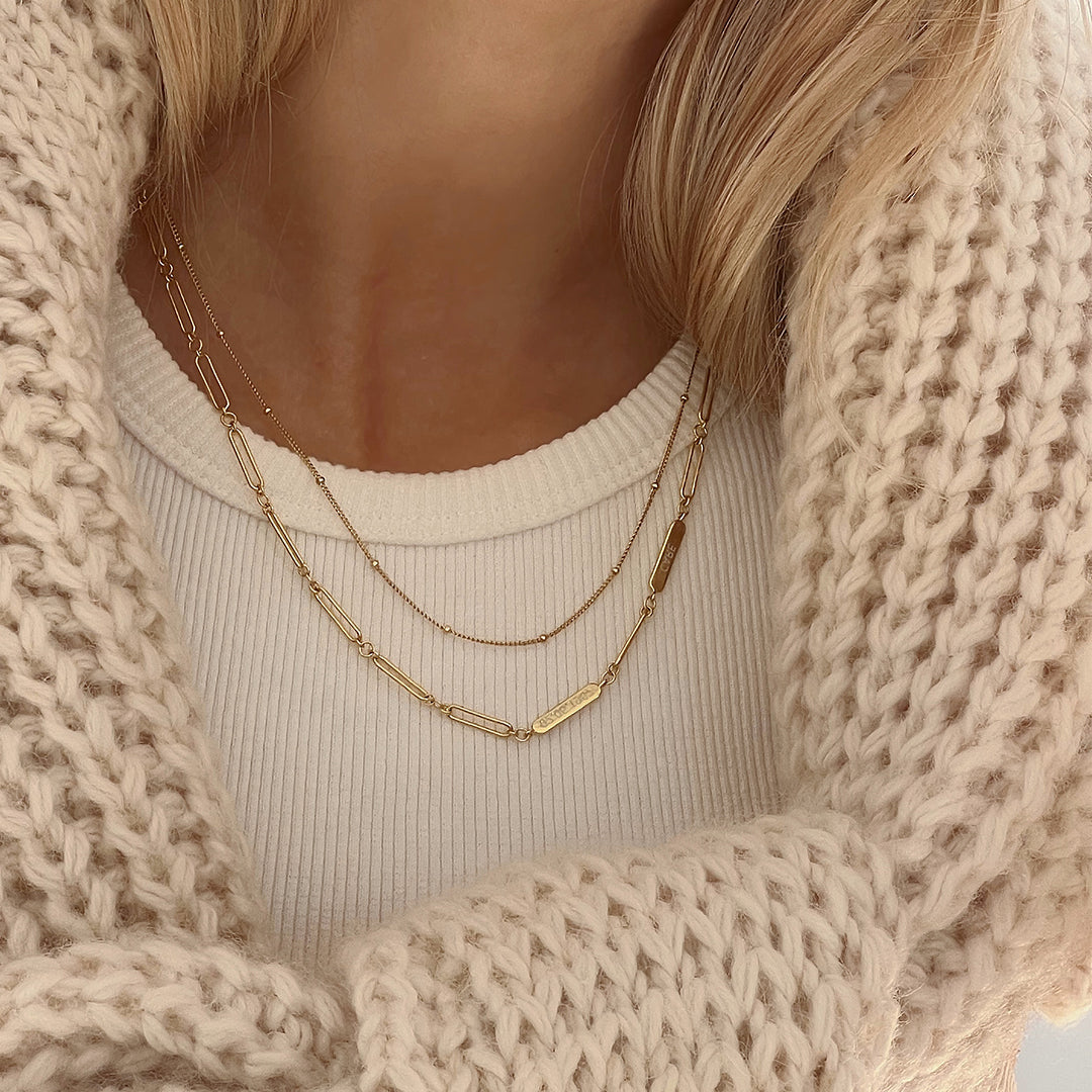 A gold chain necklace with two engraveable panels close up on around the neck