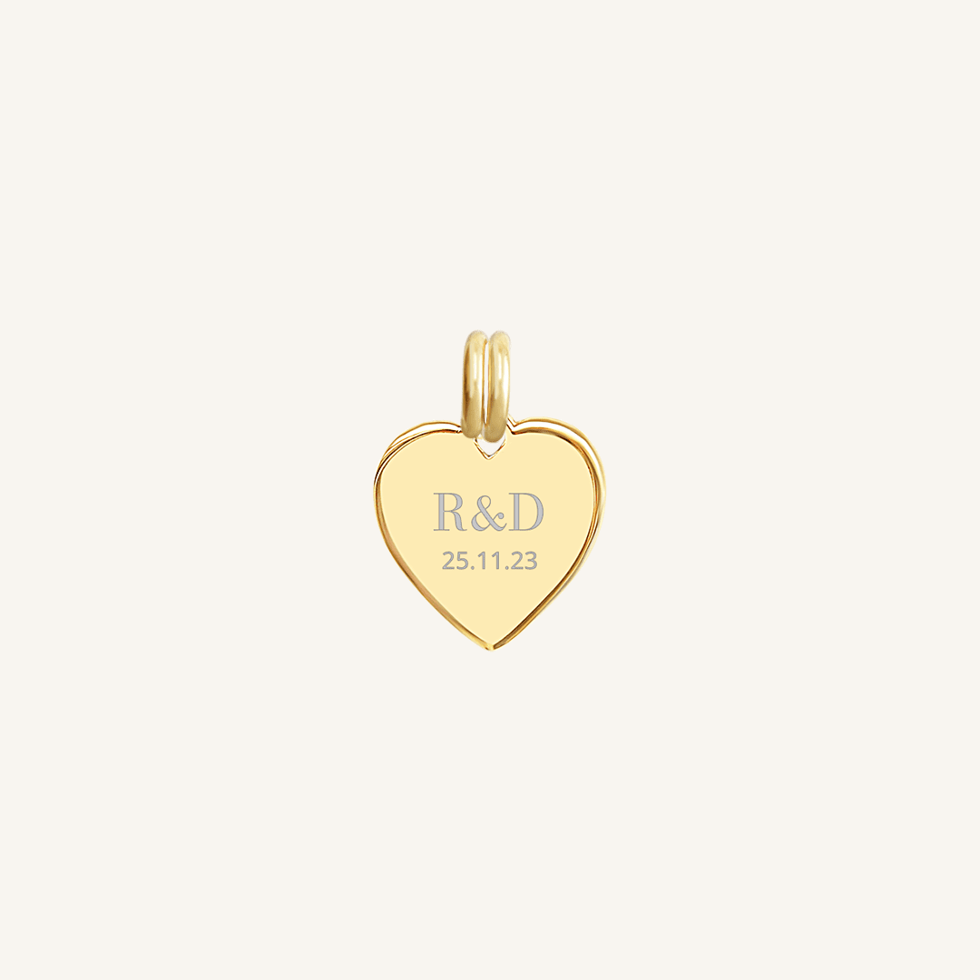 A gold heart-shaped charm with engraved initials and a date